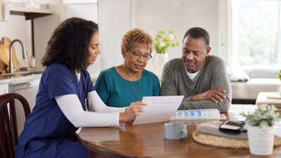 Home health professional reviewing a care plan with an older adult and family member at a kitchen table
