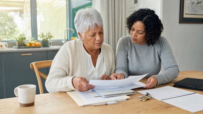 Older adult and adult child reviewing senior housing paperwork at a kitchen table